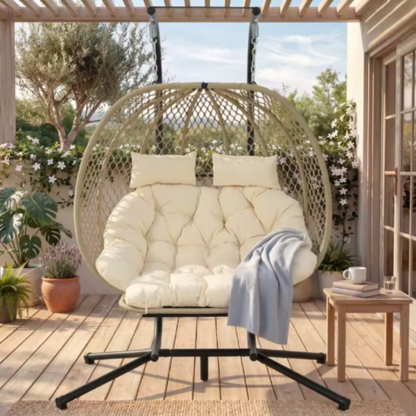 Fauteuil suspendu beige installé sur une terrasse en bois ensoleillée, décoré avec un plaid bleu et entouré de plantes.